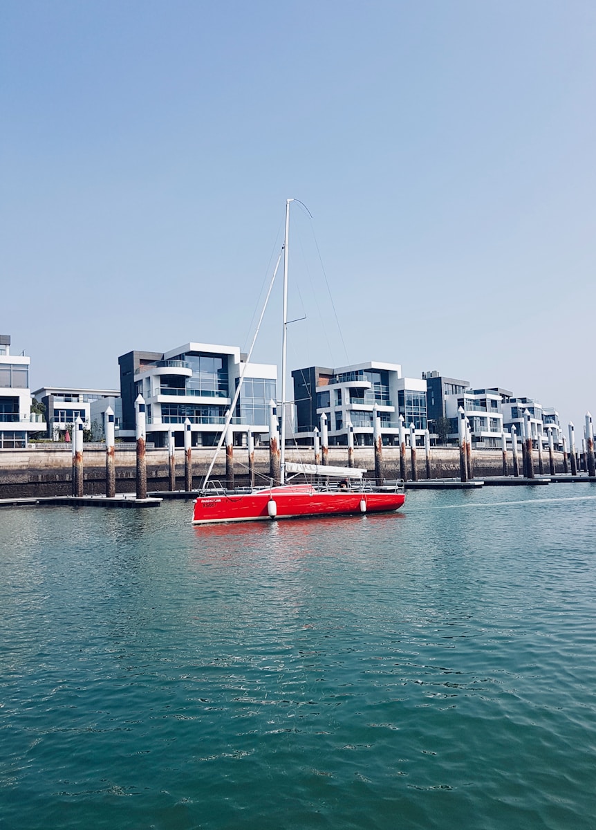 Red sailboat docked near modern waterfront buildings